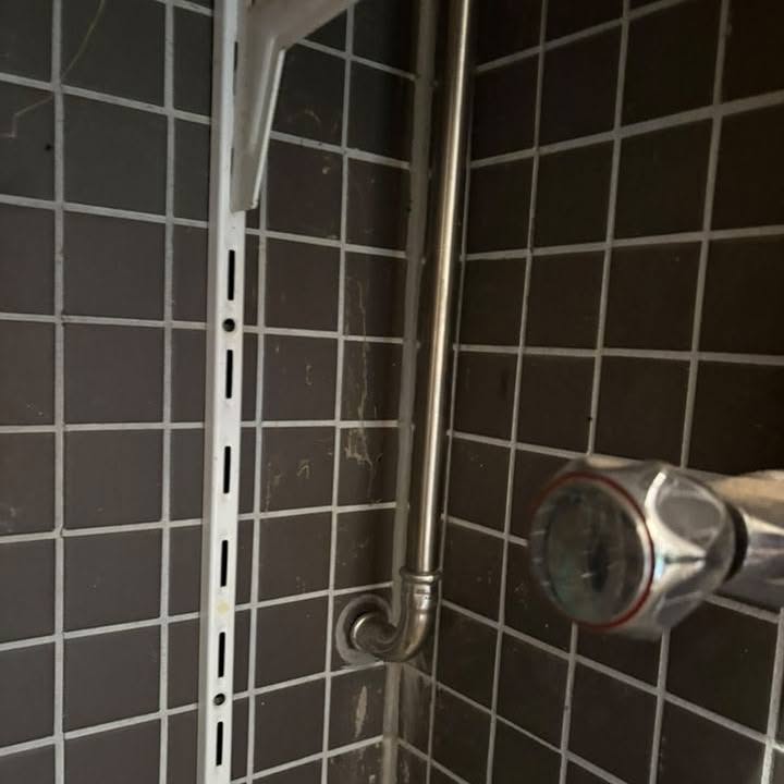 Blöndunartæki og stútar tengd í flísalögðu baðherbergi.