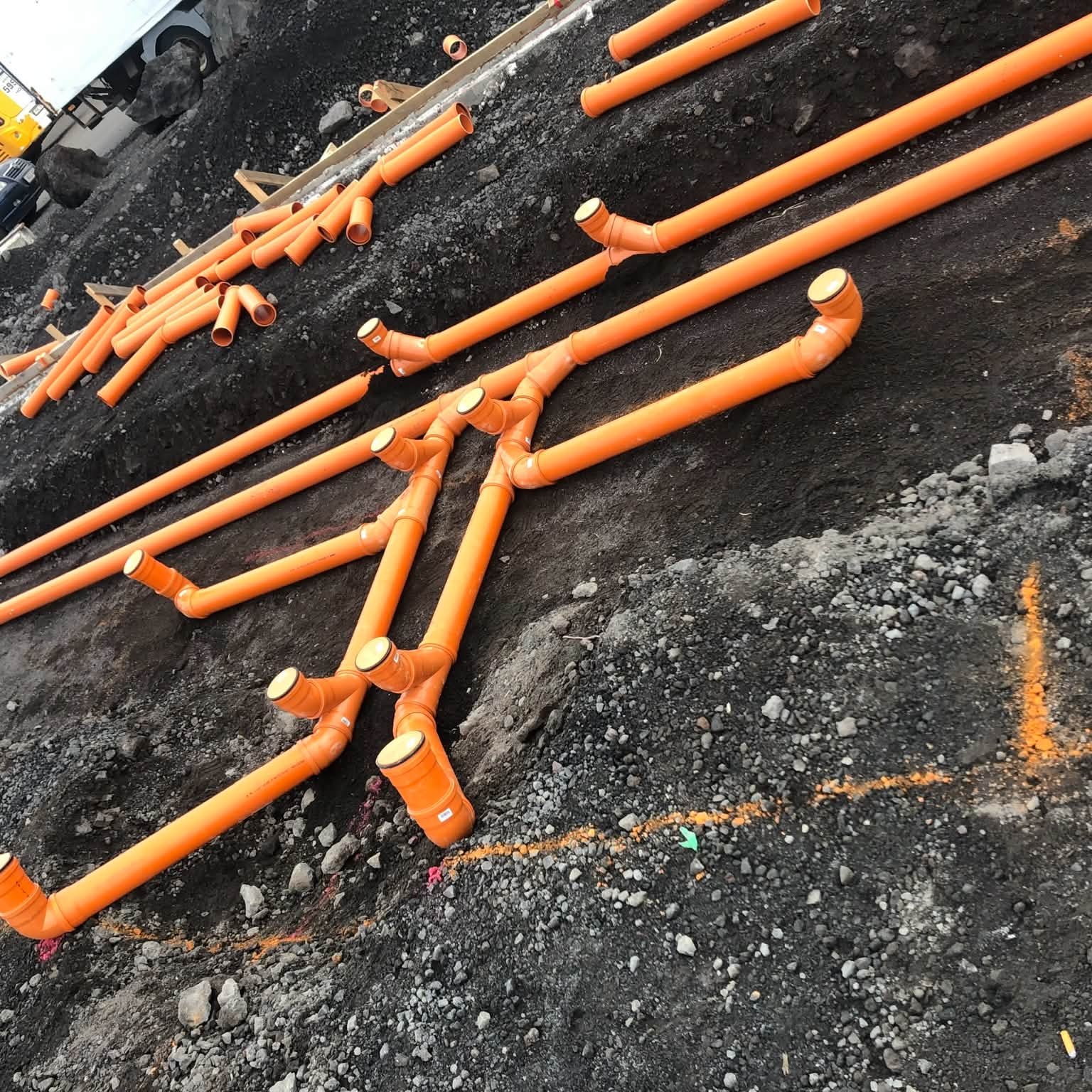 Skólplagnir úr appelsínugulu PVC lagðar og tengdar í uppgröfnum grunni.